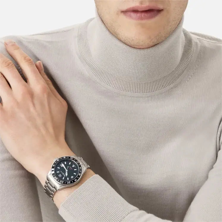 Montblanc 1858 GMT Automatic ref: 129615 herenhorloge 42mm met roestvrijstalen band en zwarte wijzerplaat, gedragen door een man met een beige coltrui.